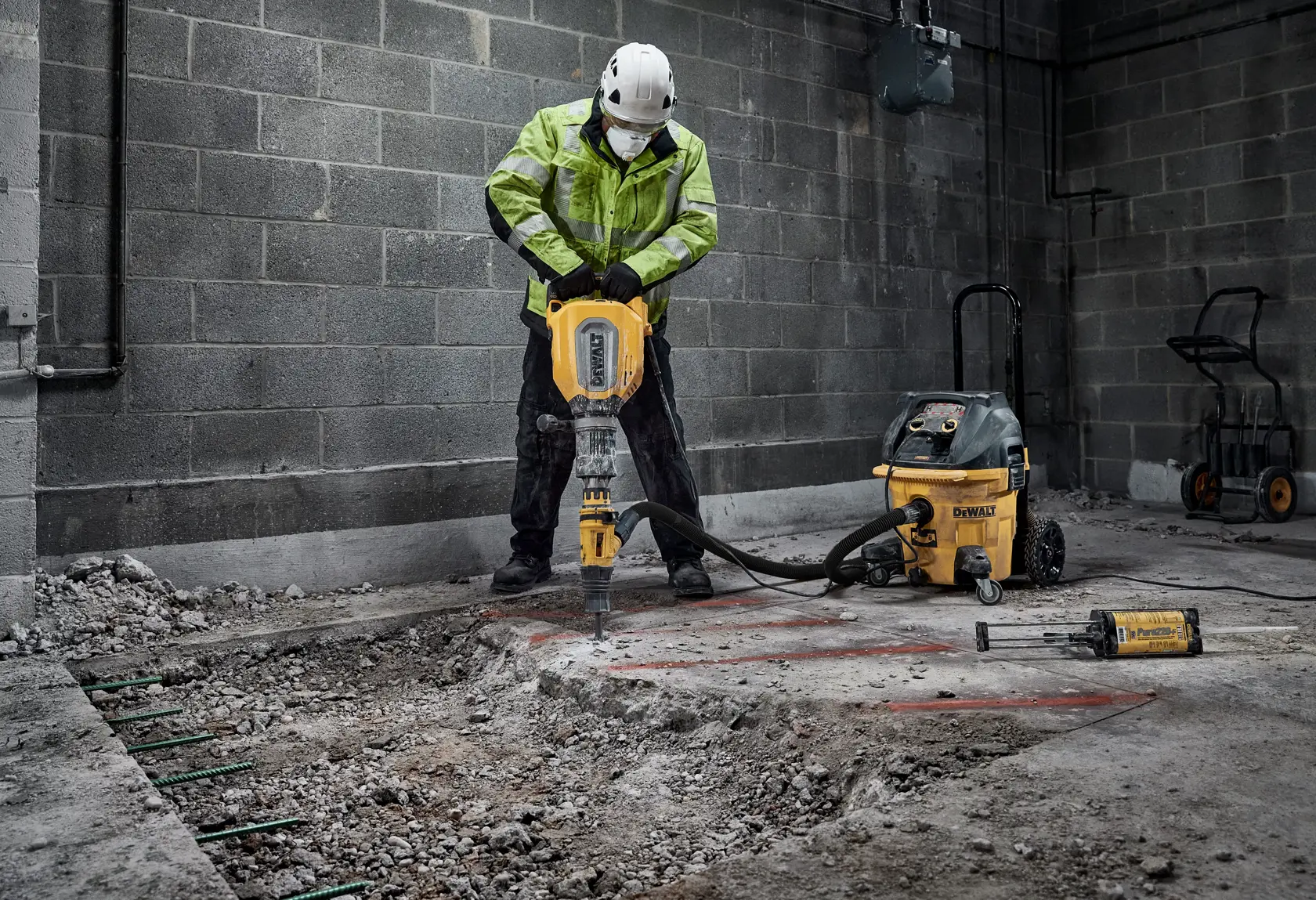 Trabajador usa martillo demoledor DEWALT para romper concreto en interior. Equipo de seguridad visible.