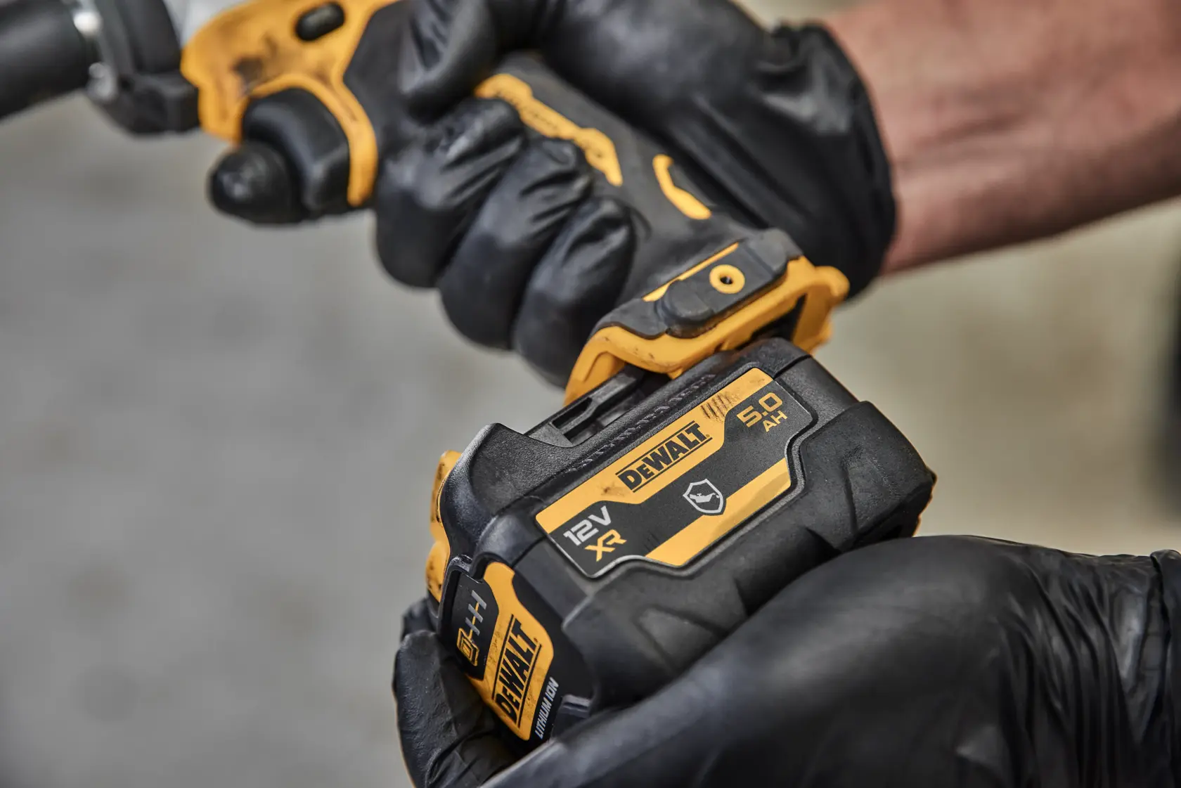 Nahaufnahme einer Person mit schwarzen Handschuhen, die einen DEWALT 12V XR 5,0Ah Akku, Modell DCB126G, an einem kompatiblen Werkzeug befestigt.
