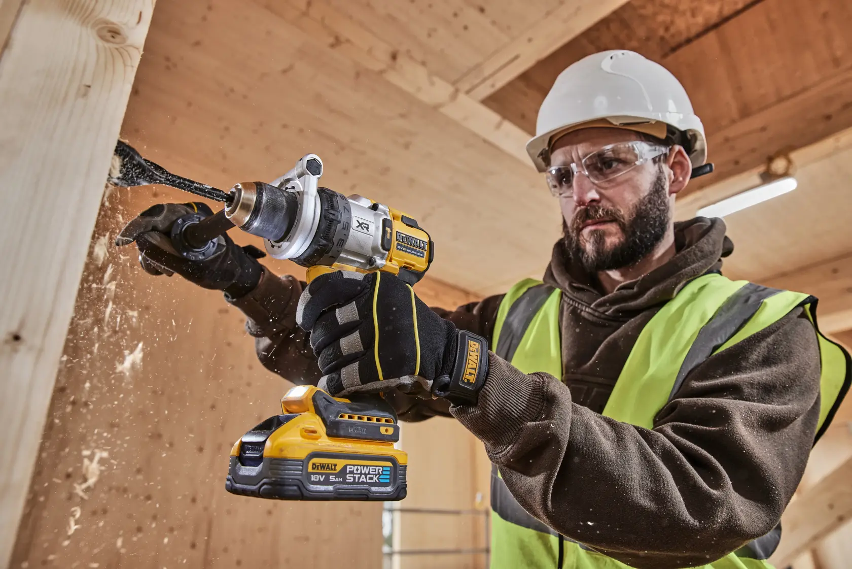 Taladro DEWALT inalámbrico usado en madera, operario con guantes, casco y chaleco reflectante.