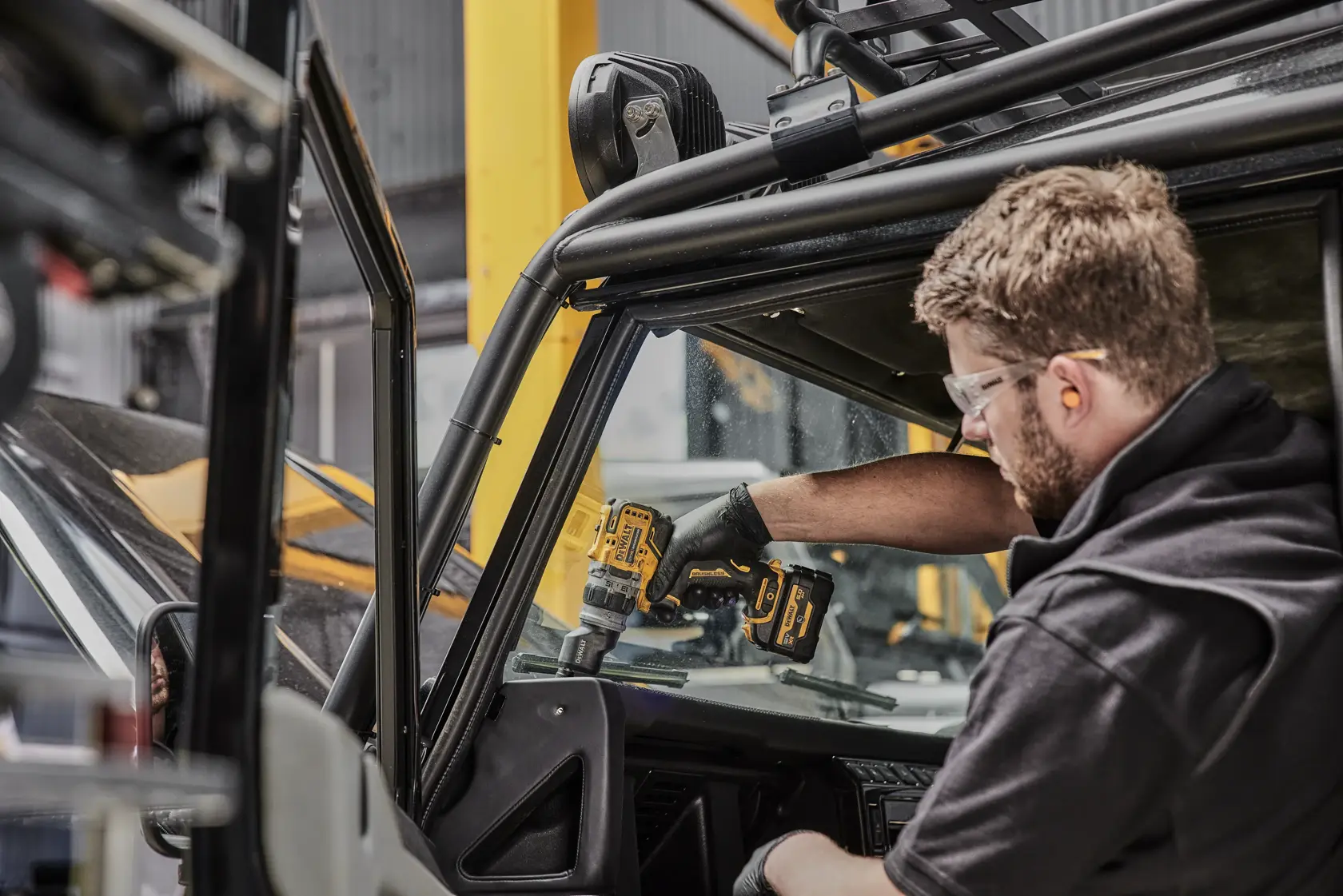 Eine Person benutzt einen kabellosen DEWALT-Bohrer im Inneren eines Fahrzeugs und arbeitet im Bereich des Armaturenbretts. Das Gesicht der Person ist aus Datenschutzgründen unscharf.