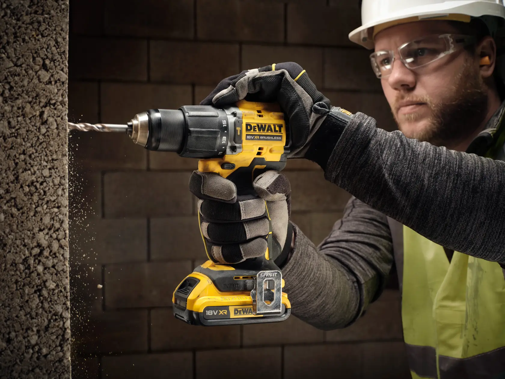 Mano enguantada perfora concreto con DEWALT DCD799D2T inalámbrico. Entorno de obra, primer plano.
