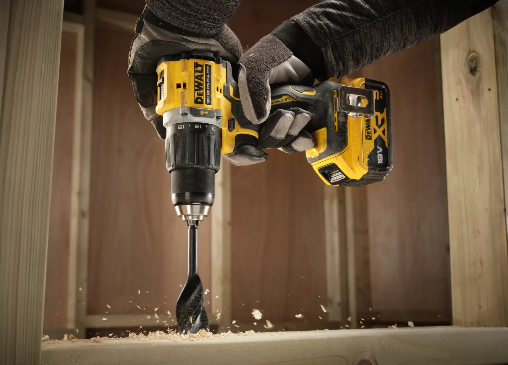 Person using a DEWALT cordless drill to bore a hole in wood, with wood shavings flying.