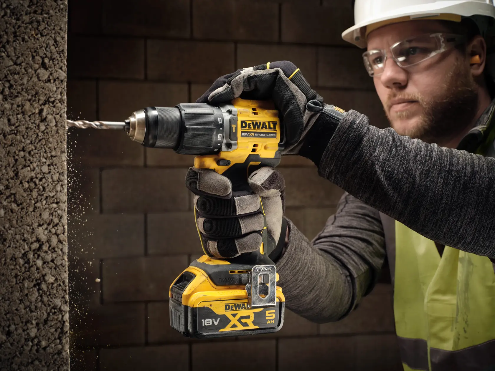 Worker uses a DEWALT DCD799N cordless drill to drill into a concrete wall. Tool is yellow and black.