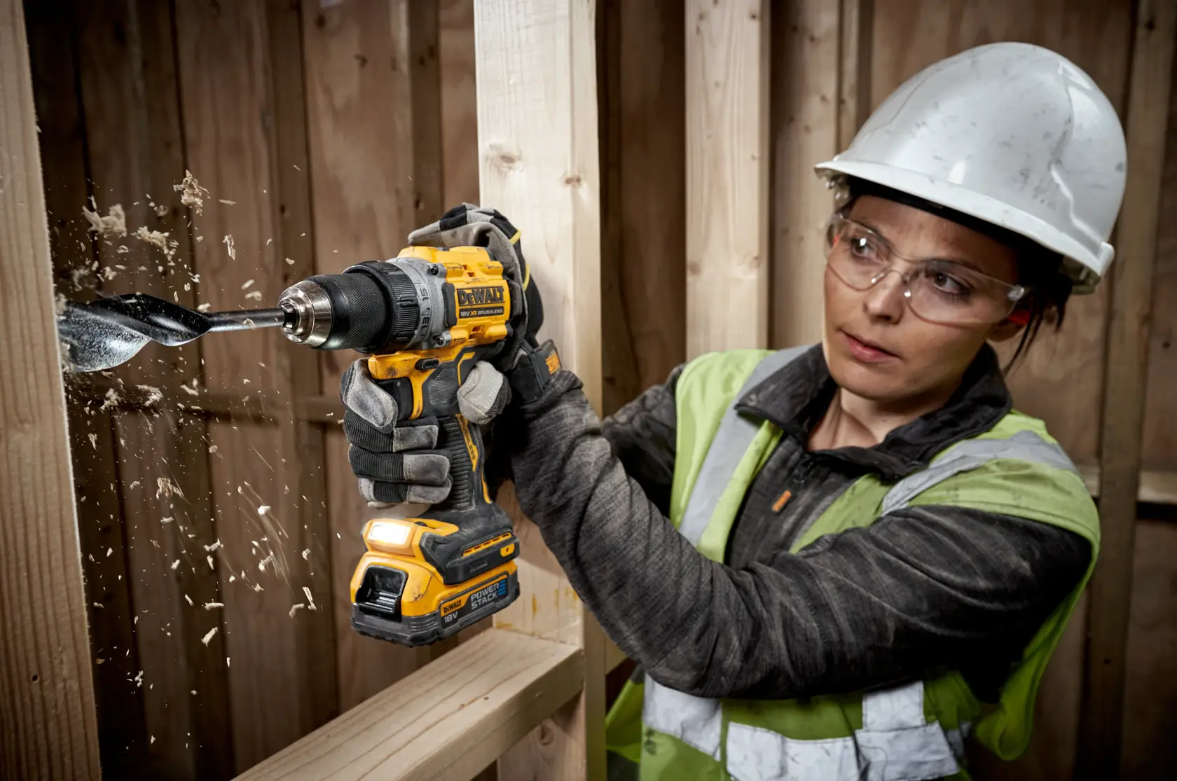 DEWALT DCD800E1T drill in use, drilling through wood with shavings flying, worker wearing gloves and helmet.