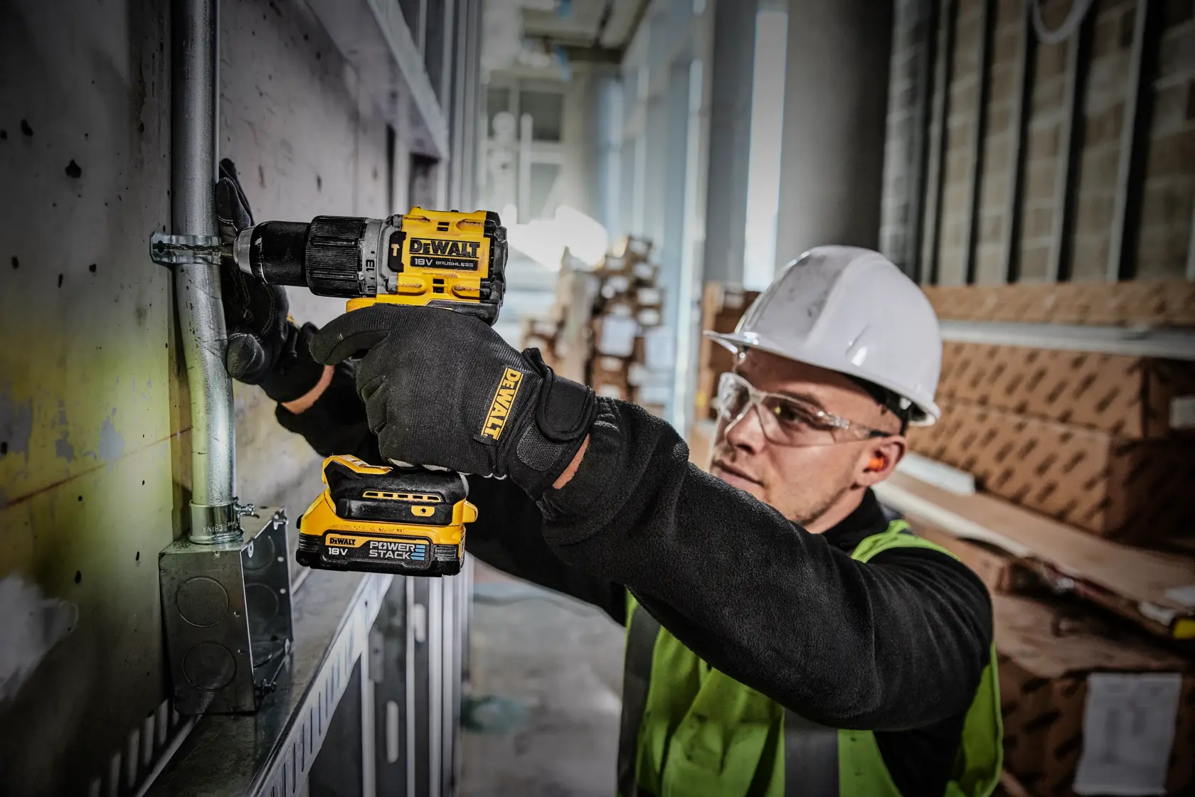 Trabajador utiliza taladro DEWALT DCD805E2T en un tubo metálico, con equipo de seguridad, en obra.