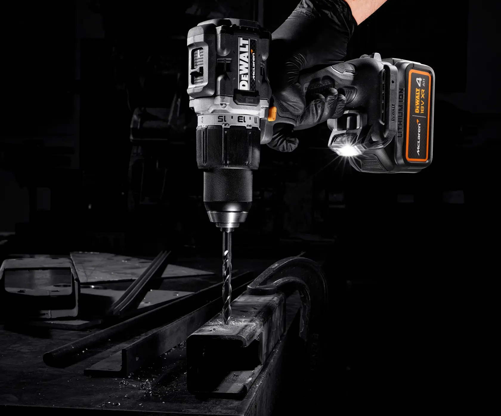 Taladro inalámbrico DEWALT perforando metal, mano con guante, luz LED encendida, taller oscuro.