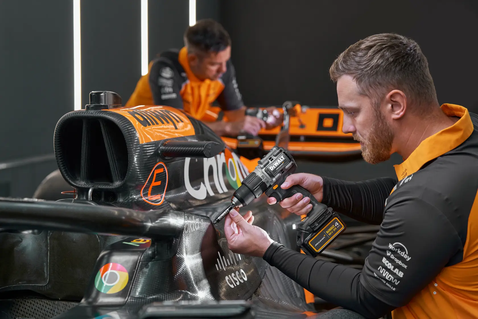 Persona usa taladro DEWALT sobre auto de carreras. Rostros difuminados, logo DEWALT visible.