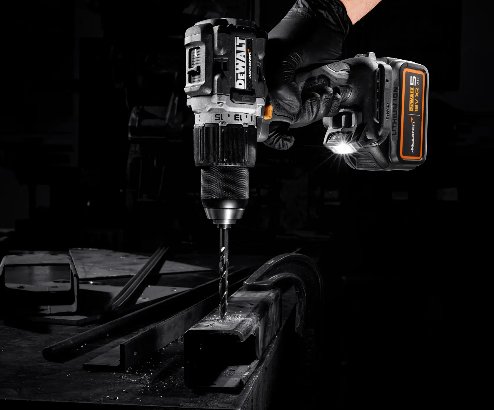 Taladro DEWALT inalámbrico sobre metal, sostenido con guante y luz LED iluminando el área de trabajo.