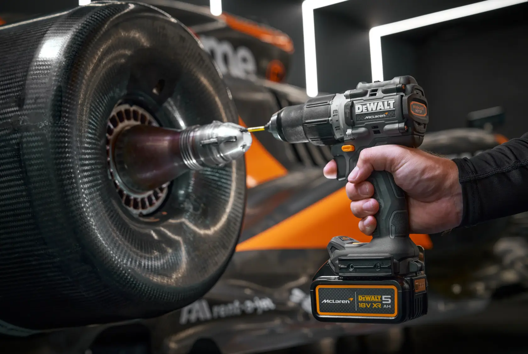 Mano usando taladro DEWALT en rueda de coche de carreras. Logotipo de McLaren visible en la herramienta.