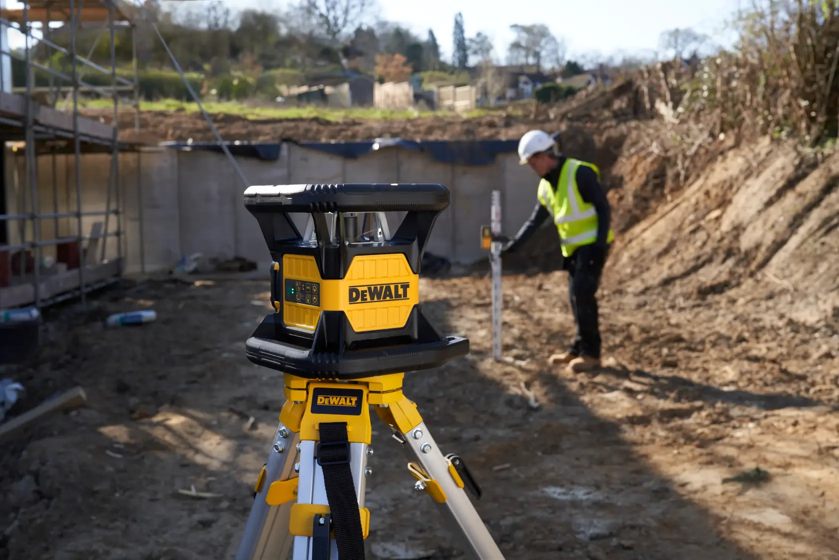 DEWALT-Laser auf Stativ an Baustelle, im Hintergrund ein Arbeiter mit Sicherheitskleidung und Ausrüstung.