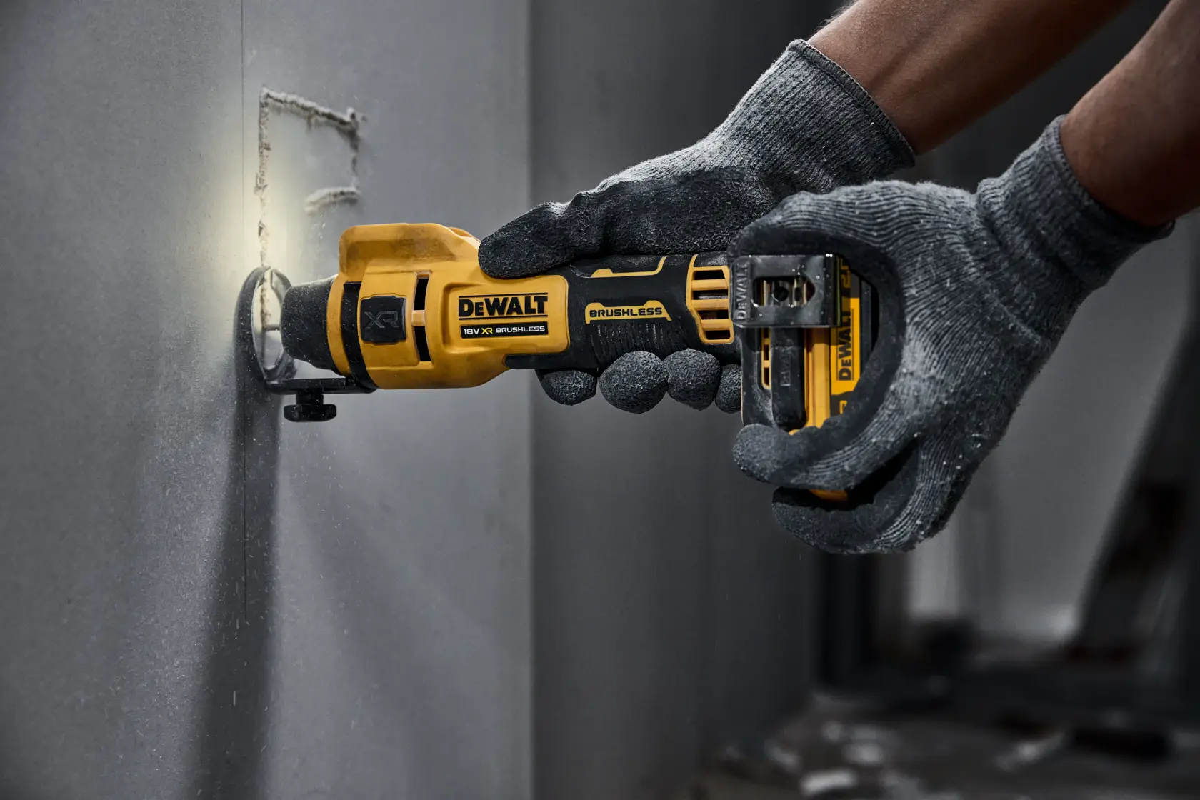 Herramienta rotativa inalámbrica DEWALT cortando panel de yeso, manejada con guantes.