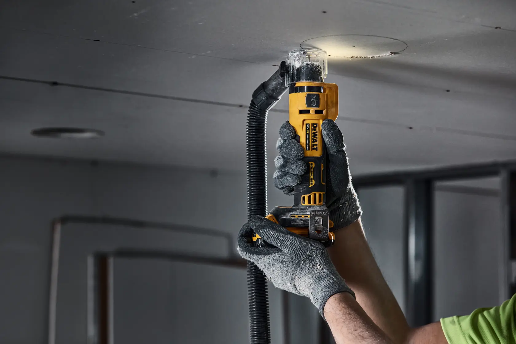 Mano usando herramienta DEWALT para cortar un agujero circular en un panel de techo.