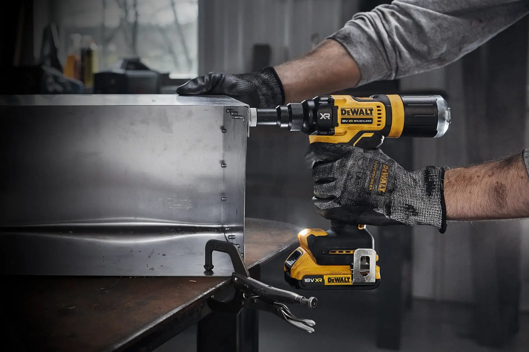 Una persona con guantes de trabajo usa una herramienta eléctrica inalámbrica DEWALT DCF403NT para atornillar tornillos en una caja de metal en un taller.