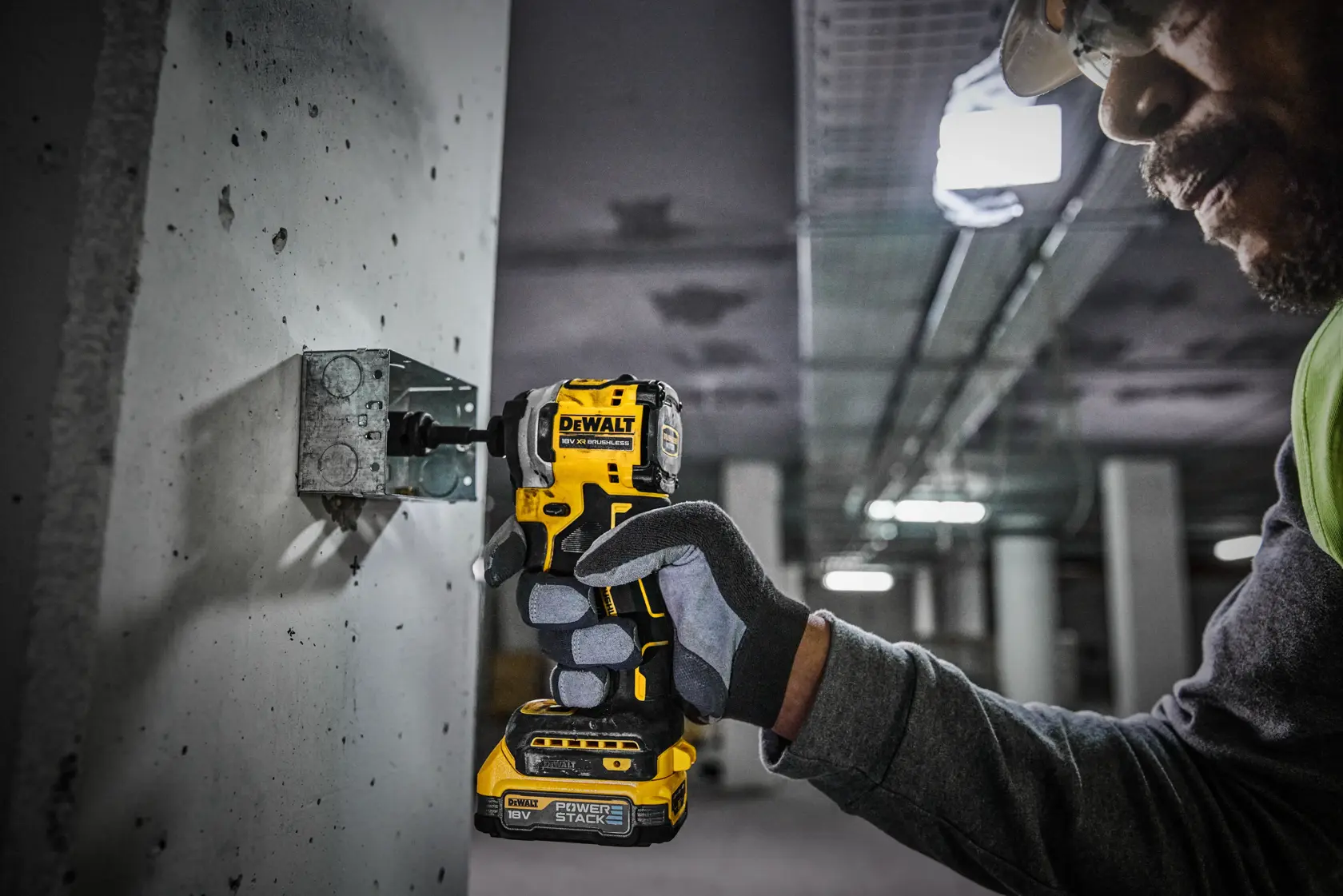 Una persona con guantes de seguridad utiliza un atornillador de impacto inalámbrico DEWALT (modelo DCF850) para fijar un tornillo en una pared de hormigón en un entorno industrial o de construcción.