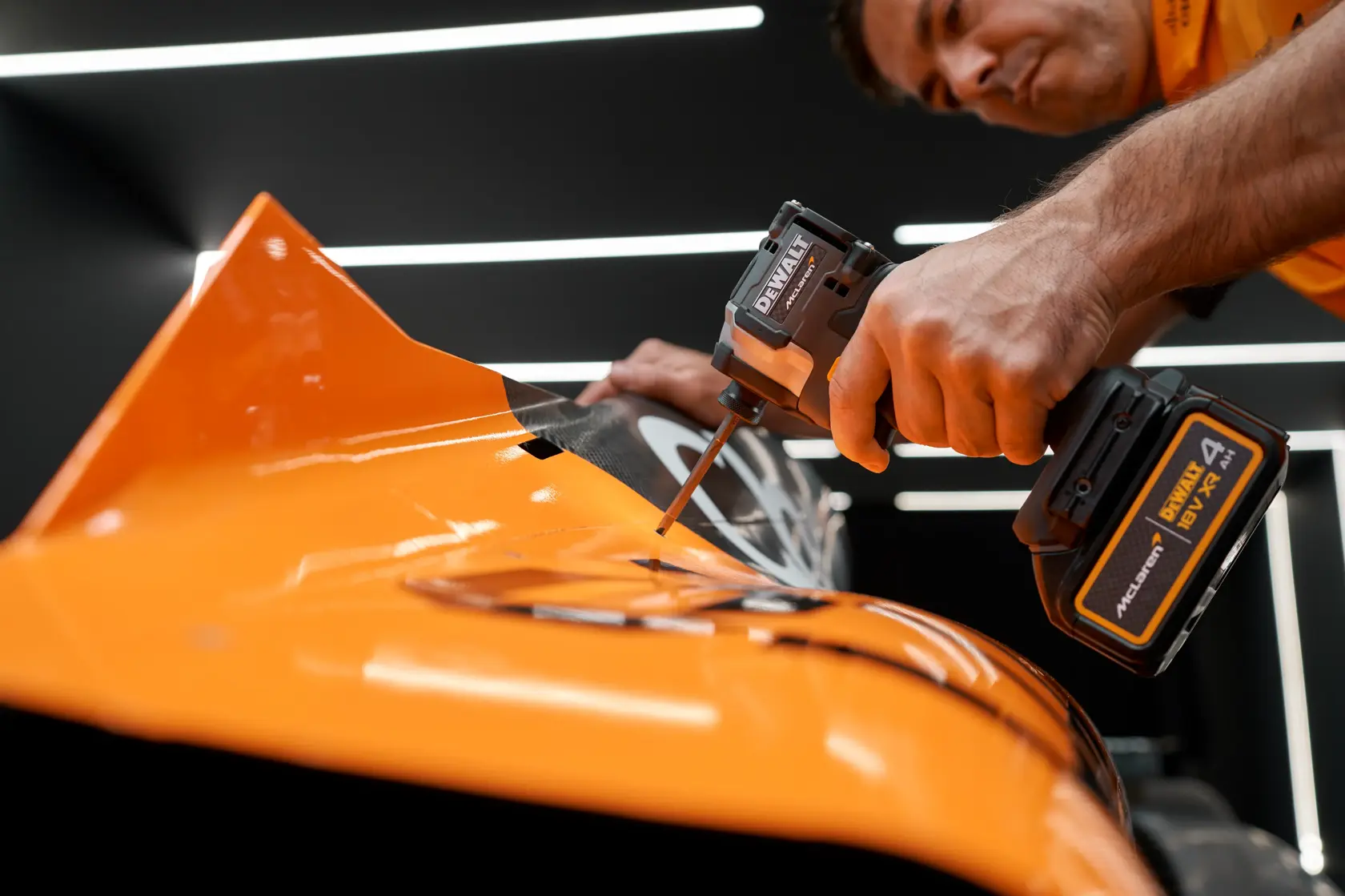 Person using a DEWALT cordless tool on an orange surface in a workshop setting.