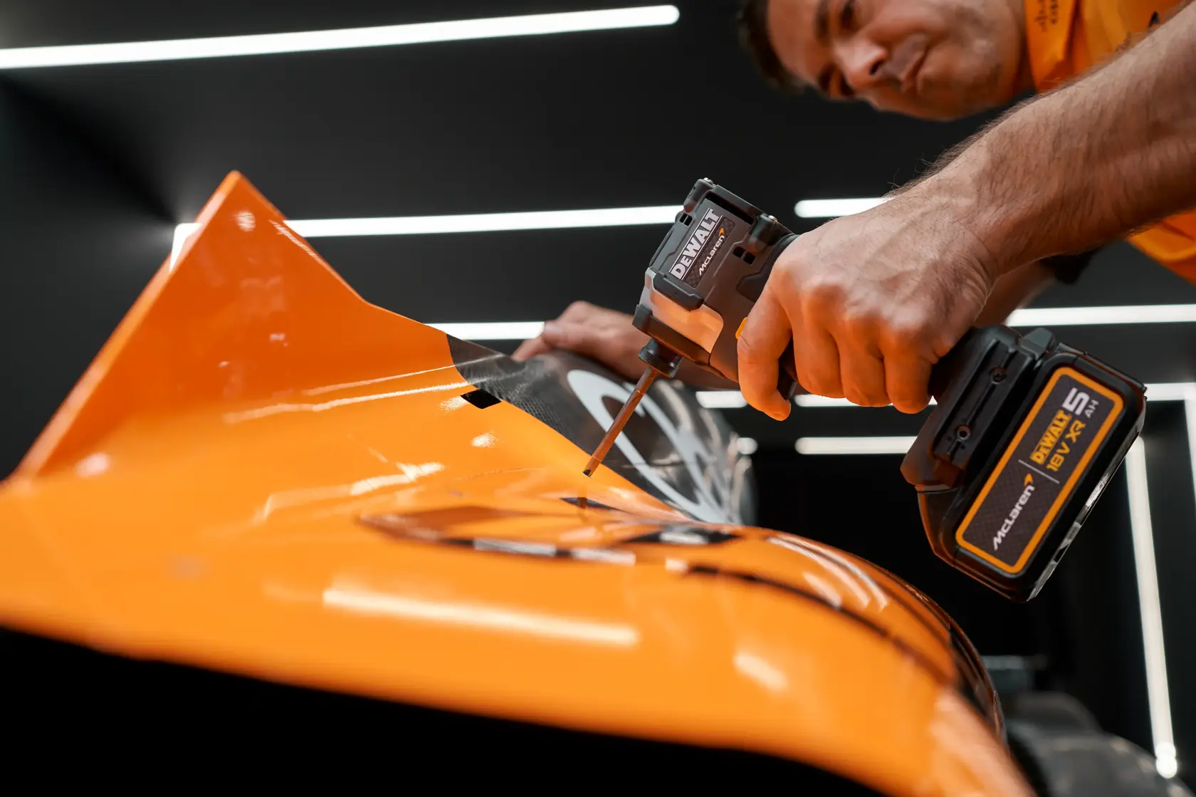 Hand using DEWALT cordless screwdriver on orange metal surface under bright lights, close-up view.