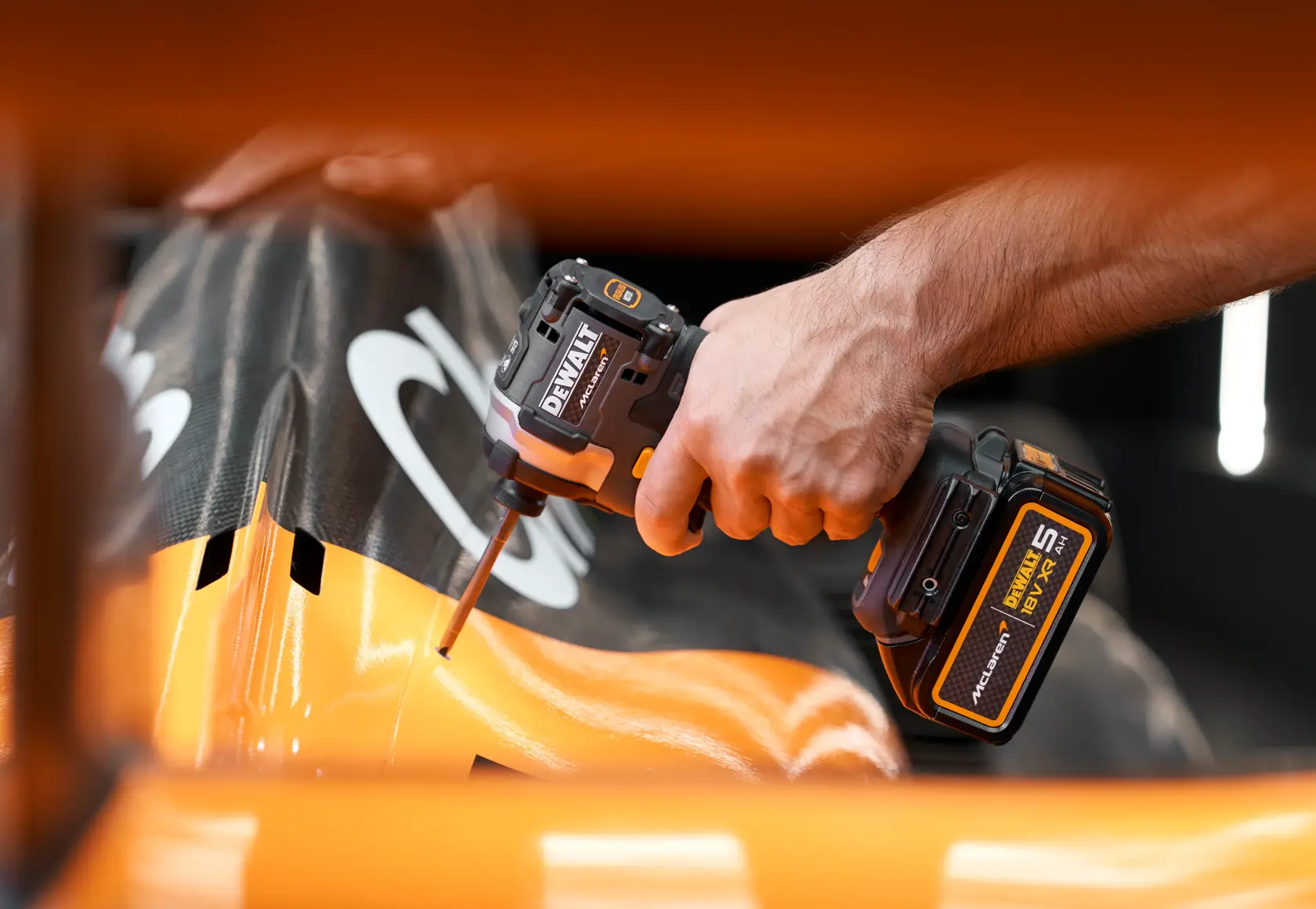 Hand using DEWALT cordless impact driver on orange and black machinery part.