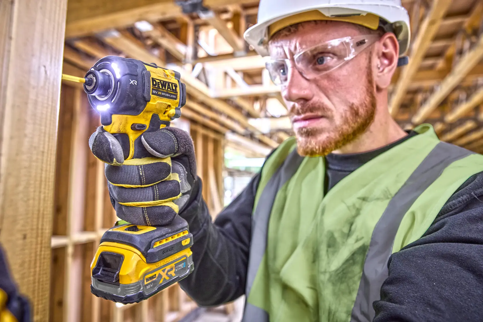 Worker using a DEWALT DCF870N impact driver in a construction site, wearing safety gear and gloves.