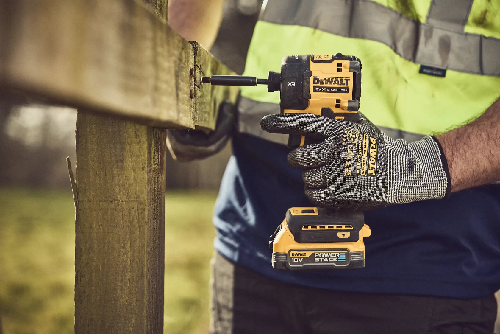 DEWALT DCF870N cordless impact wrench used to fasten a screw in outdoor wooden fencing.