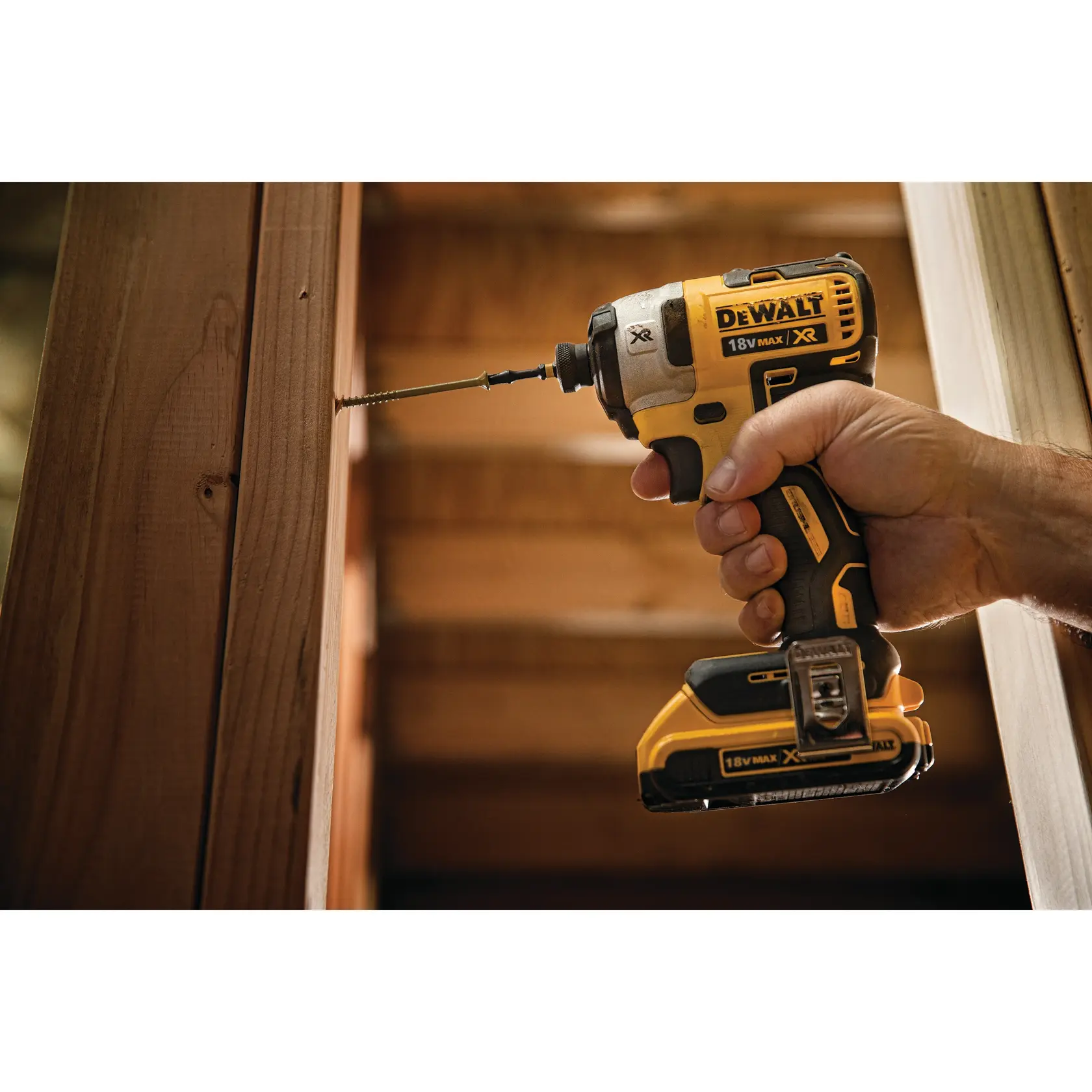 A hand holding a DEWALT 18V cordless impact driver while drilling a screw into a wooden beam.