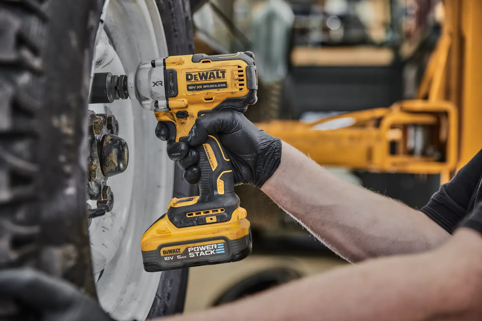 Una persona utiliza una llave de impacto inalámbrica DEWALT DCF891H2T para aflojar los pernos de una rueda de vehículo grande. La herramienta es amarilla y negra y el usuario lleva guantes negros.