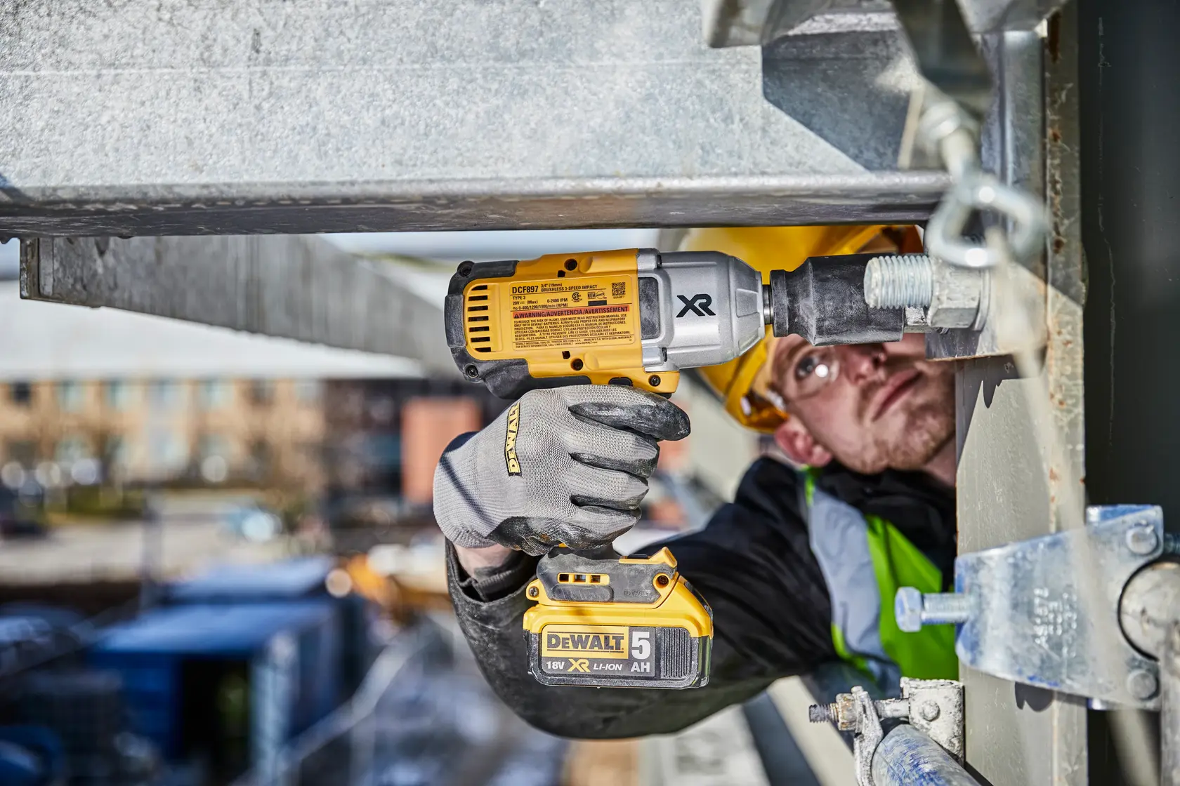 Photo of DEWALT impact wrench DCF897N-XJ, DCF897N used by worker tightening large bolt on metal frame outdoors.