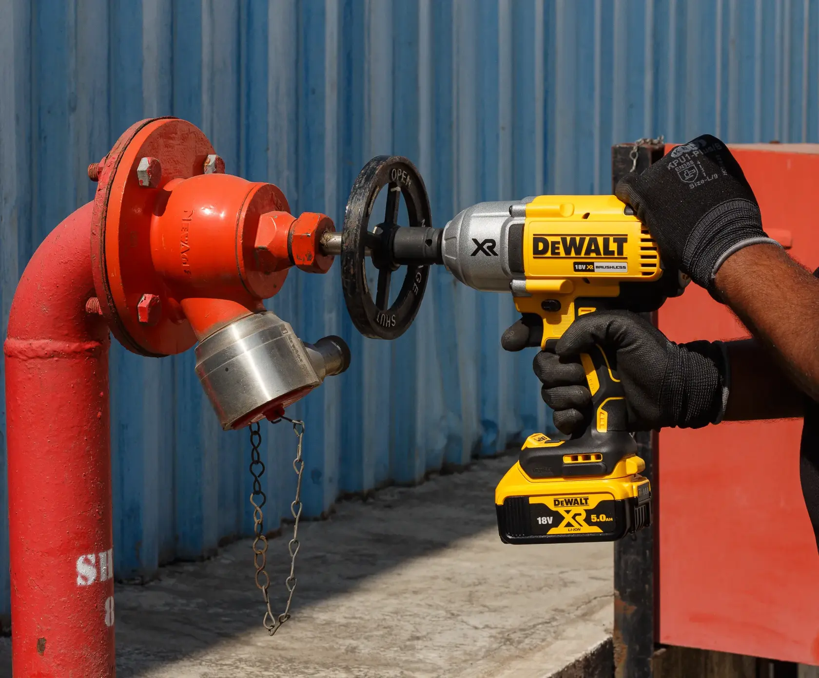 Une personne utilise une clé à choc DEWALT sans fil pour tourner la valve d’une borne d’incendie rouge.