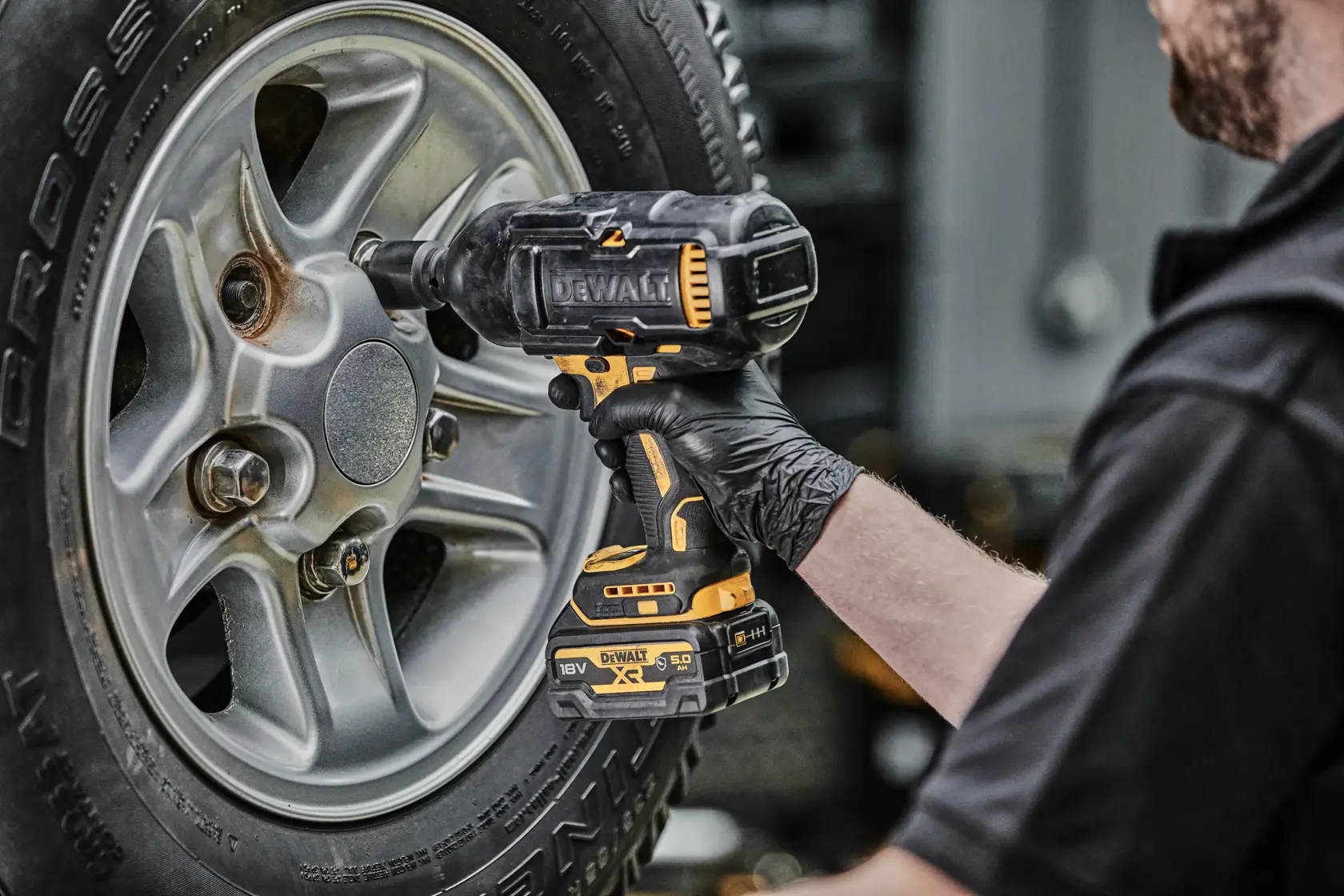 Person zieht mit einem kabellosen DEWALT Schlagschrauber einen Radbolzen am Auto fest.