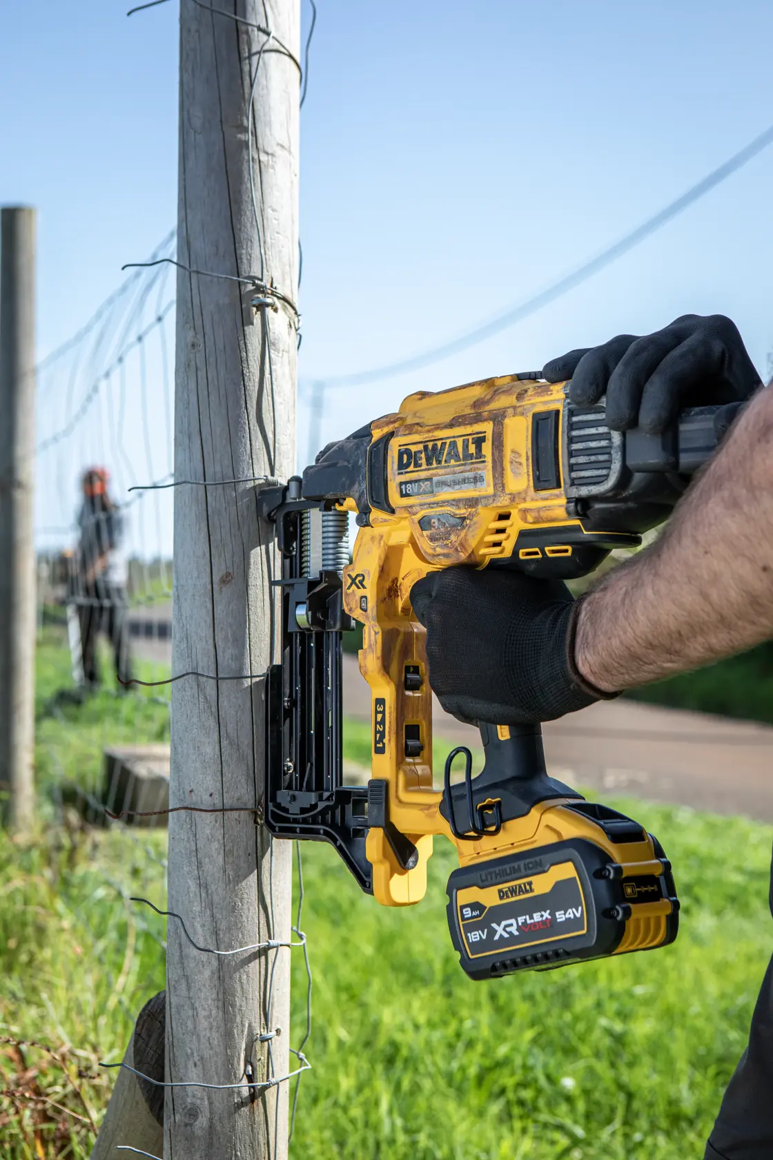 Engrapadora inalámbrica DEWALT fija alambre a un poste de madera exterior.