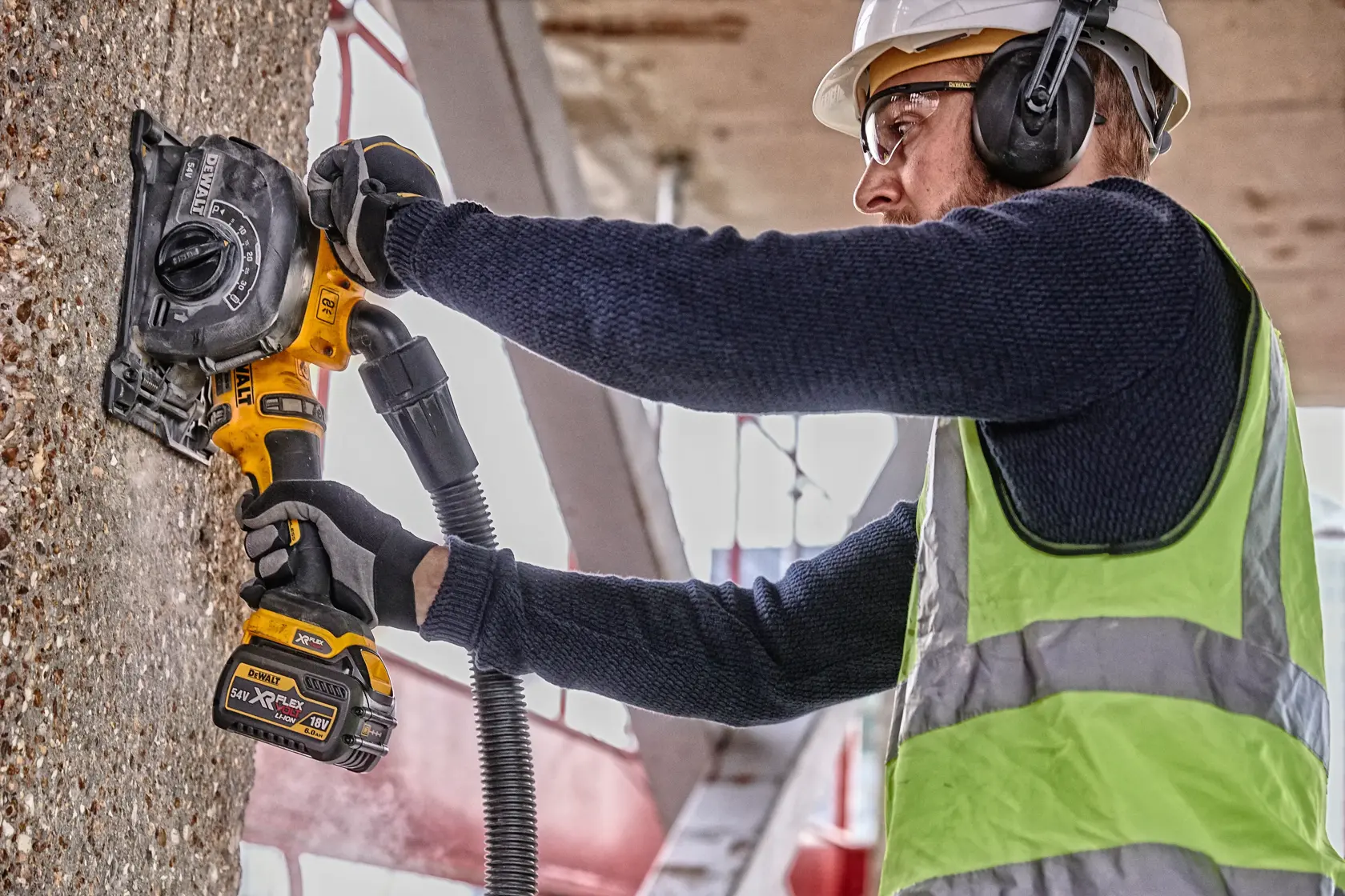 Una persona con equipo de seguridad utiliza una herramienta DEWALT inalámbrica para realizar canales en una pared de concreto en un sitio de construcción.