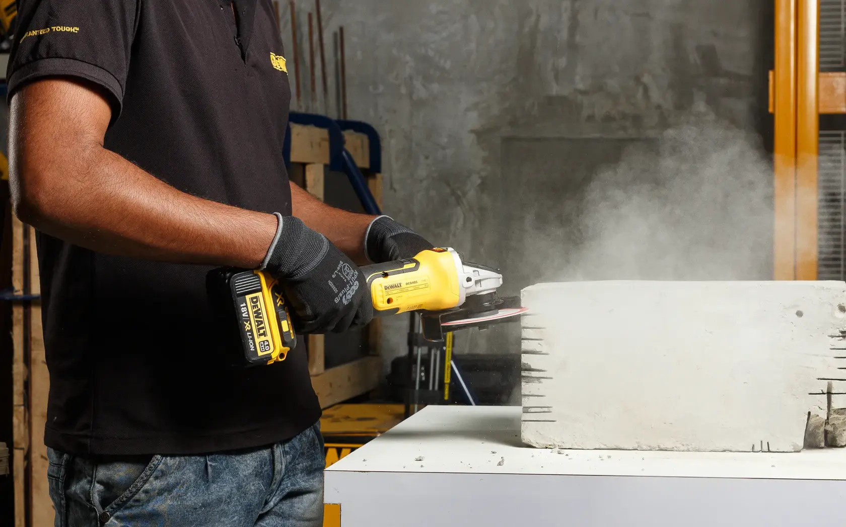 Persona usa una amoladora inalámbrica DEWALT en un bloque de concreto, generando polvo.