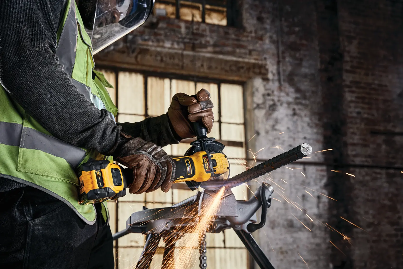 Worker uses DEWALT cordless grinder, cutting metal rod with sparks flying in industrial setting.