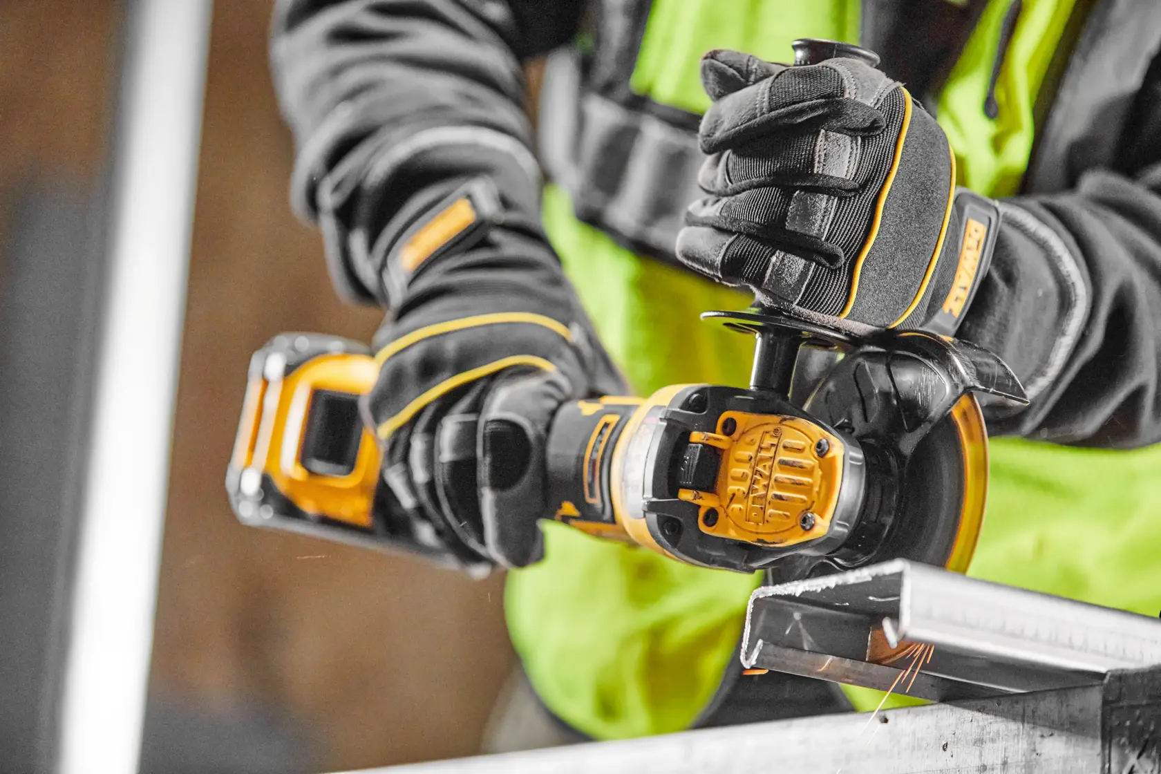 Gloved hands using a DEWALT cordless grinder on a metal piece, worker wearing a safety vest.
