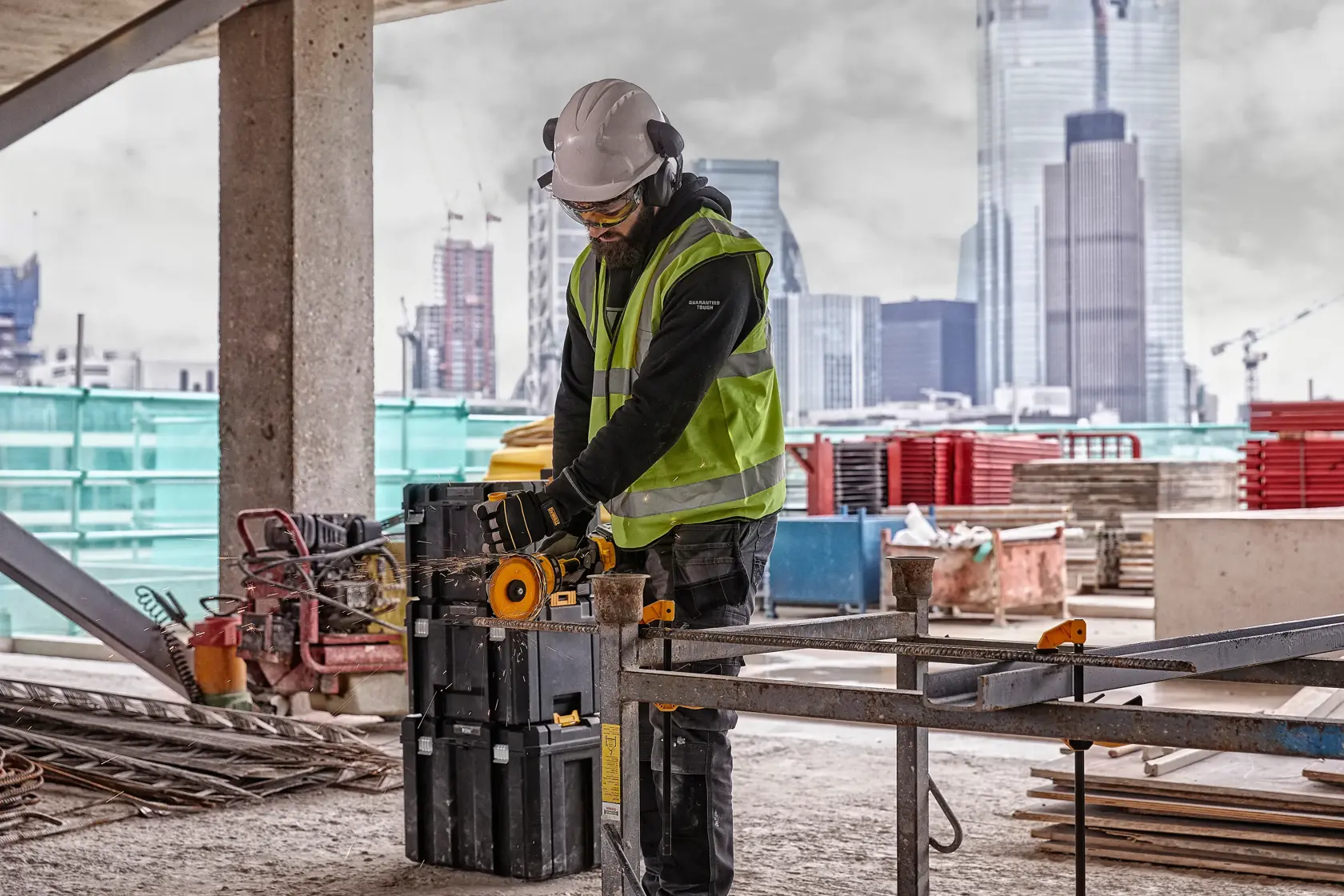 Trabajador usa herramienta DEWALT DCG418T2 en obra con edificios de fondo.
