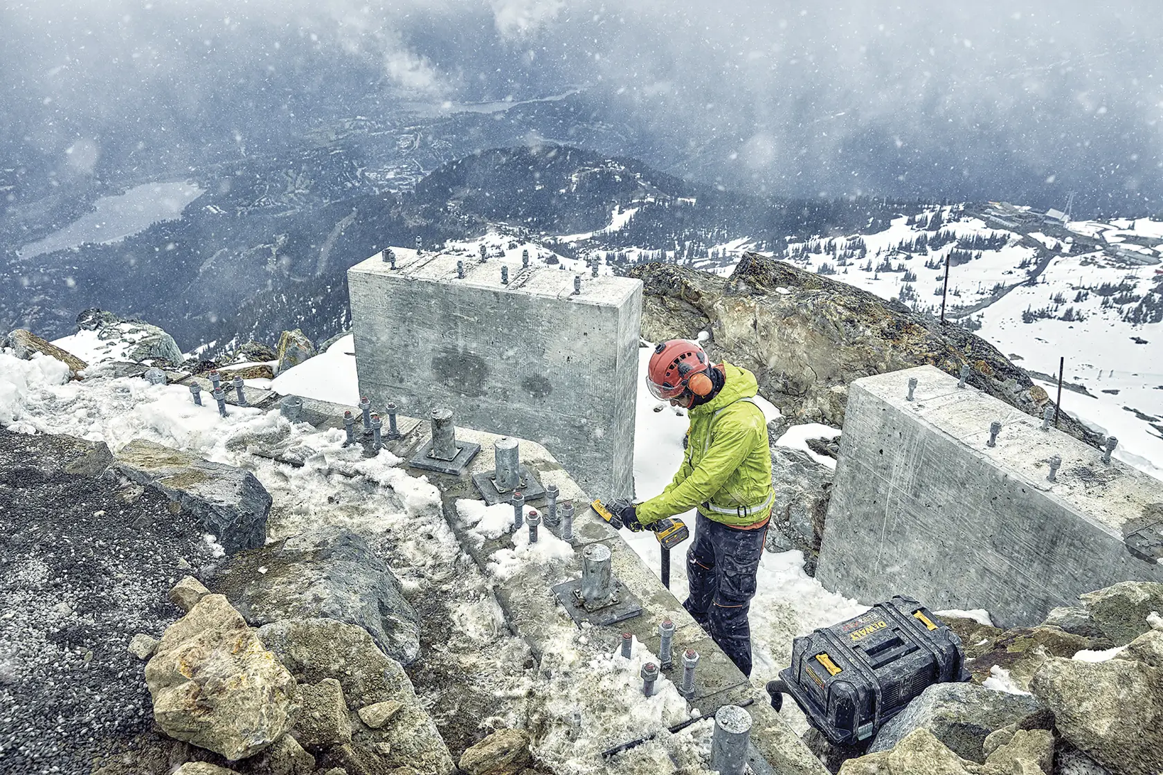 Trabajador usa herramienta DEWALT al aire libre, cerca de bloques de concreto y maleta DEWALT en zona nevada.