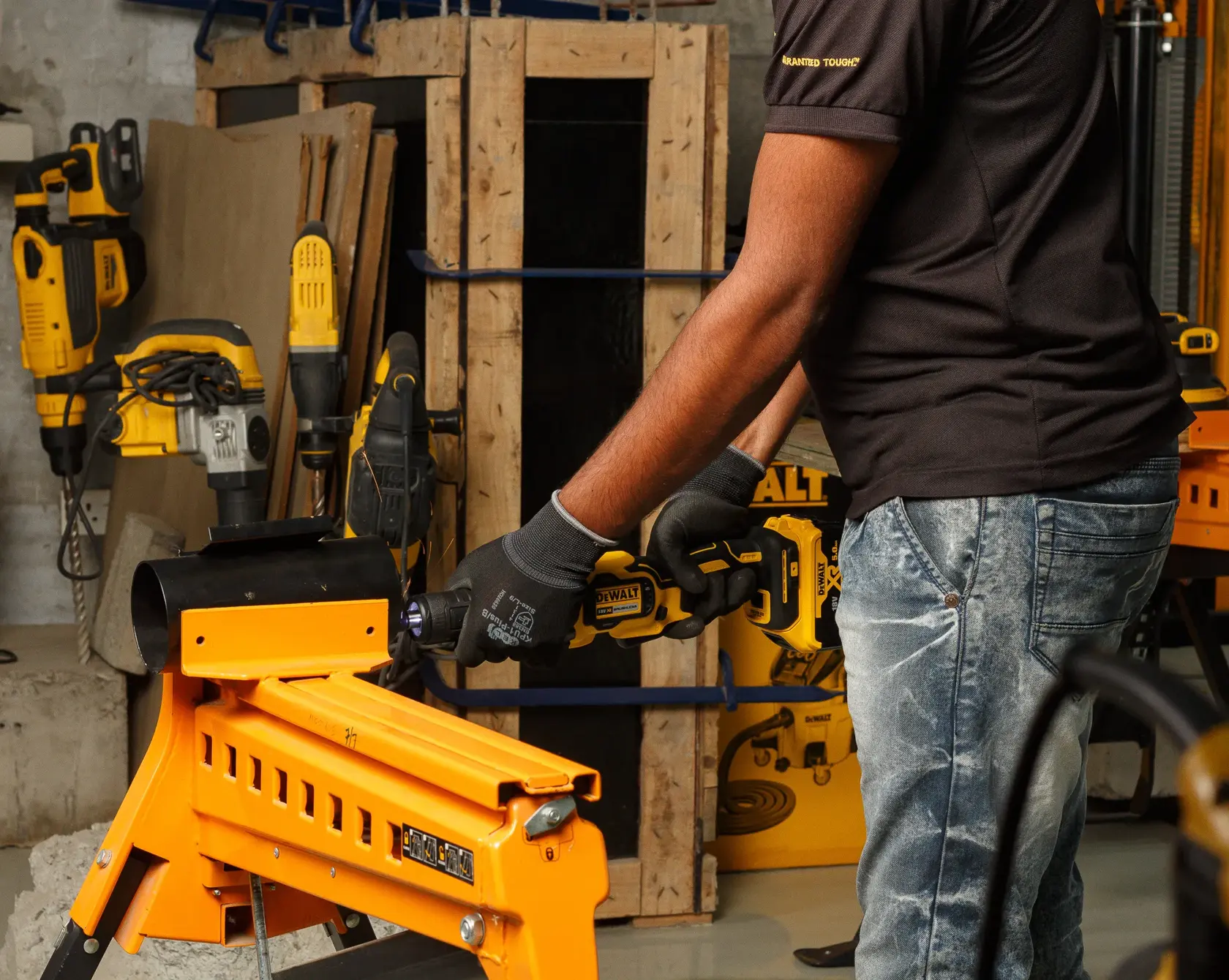 Person uses DEWALT DCG426P2 tool on orange workbench in workshop with other power tools visible in the background.