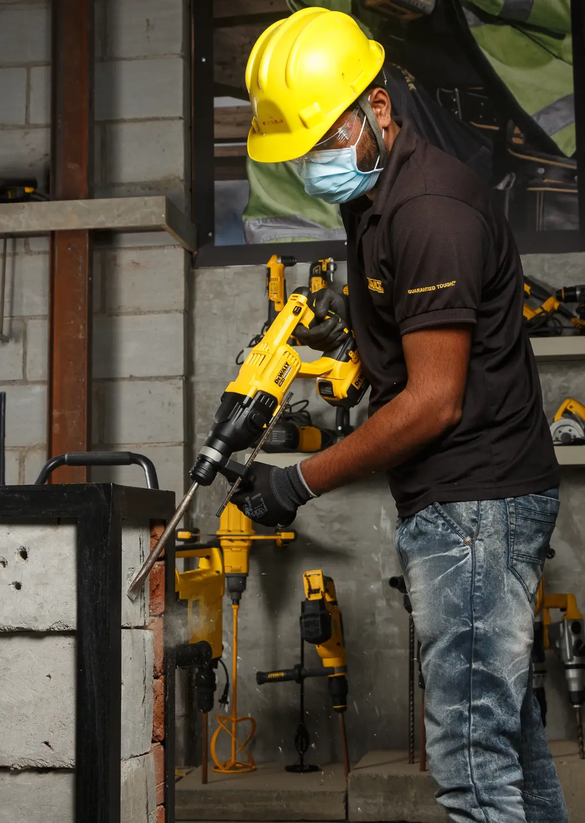 Arbeiter nutzt DEWALT DCH133NT Bohrhammer an Betonwand. Schutzkleidung und Werkzeuge sichtbar.