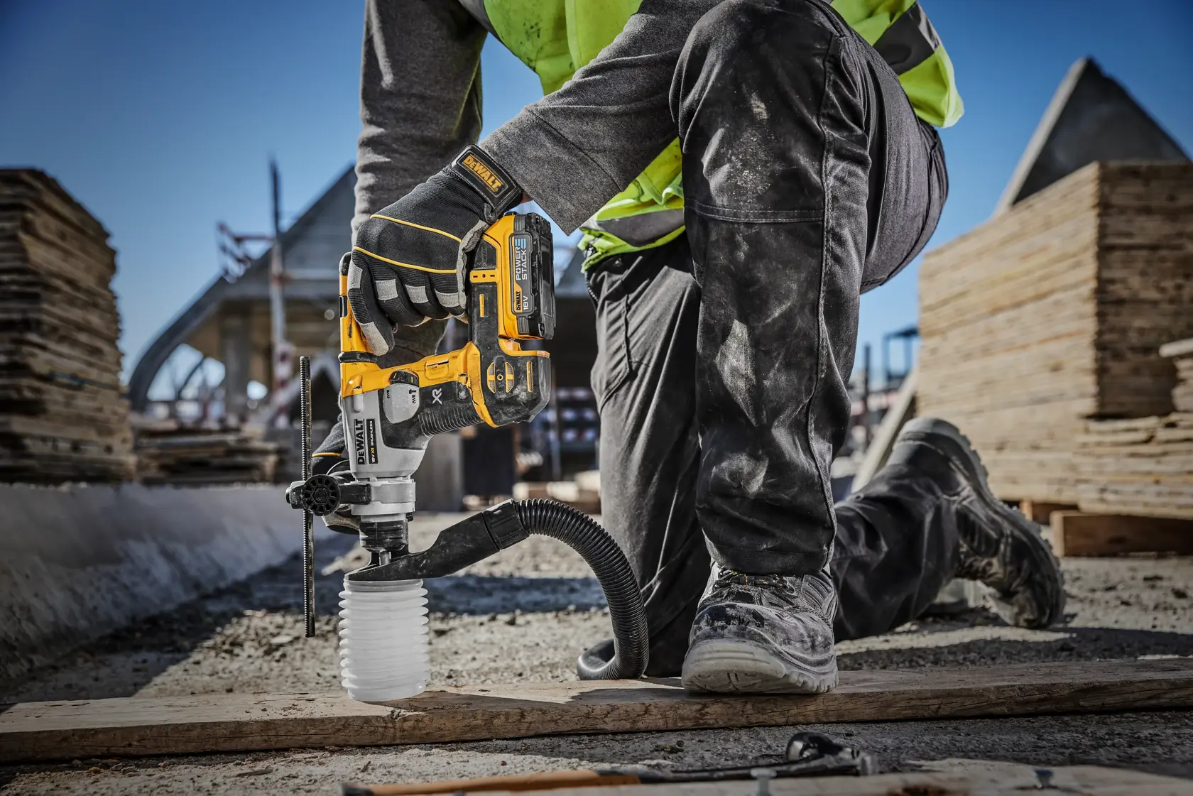 Un trabajador de la construcción está usando un martillo perforador inalámbrico DEWALT (modelo DCH172E2T) con extracción de polvo en una obra, perforando el suelo mientras se arrodilla.