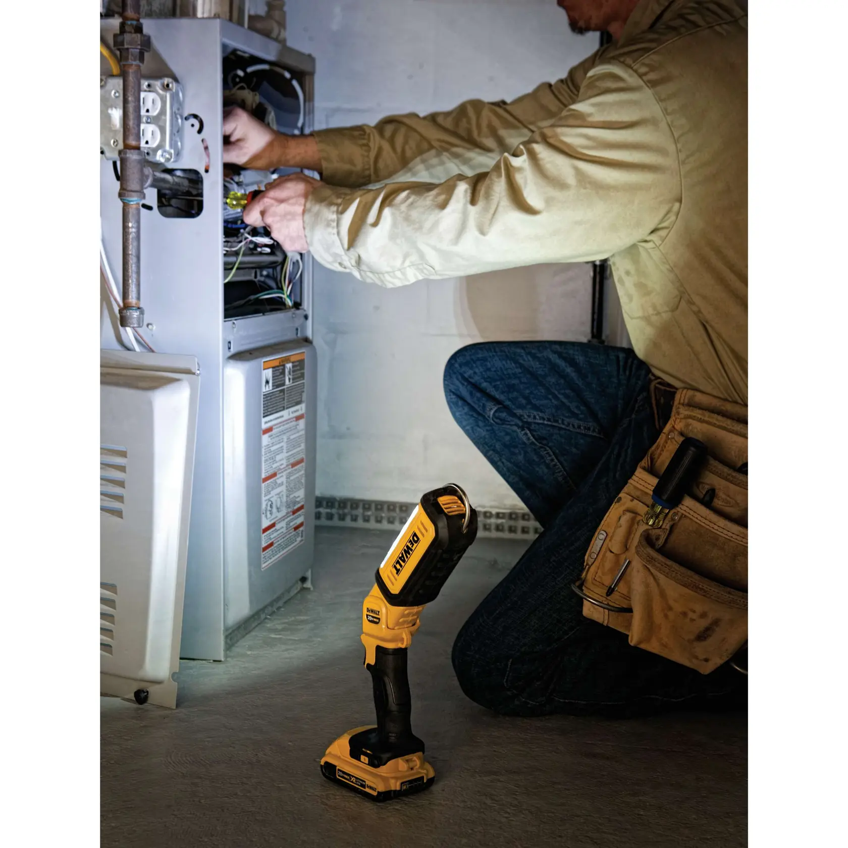 A DEWALT DCL050 LED work light is being used to illuminate an automotive suspension system while a person wearing safety glasses and gloves works with another DEWALT tool.