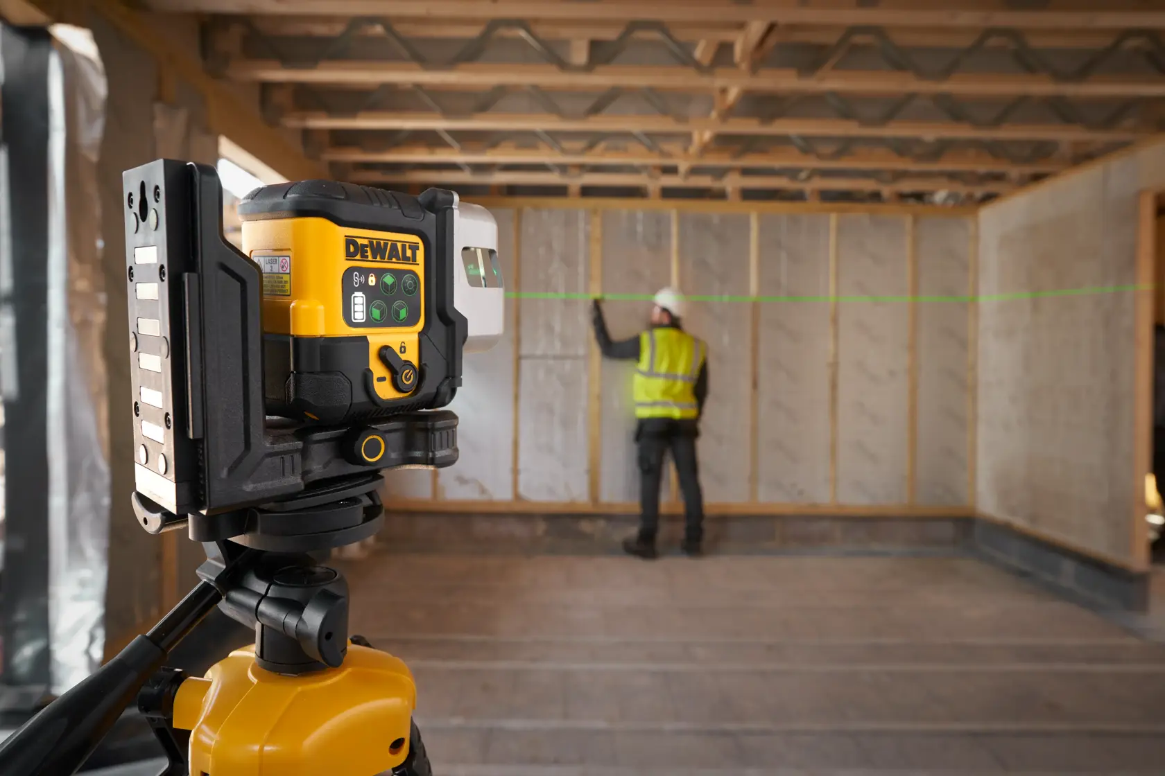 DEWALT laser level projecting a green line, used by a worker for wall alignment on a construction site.