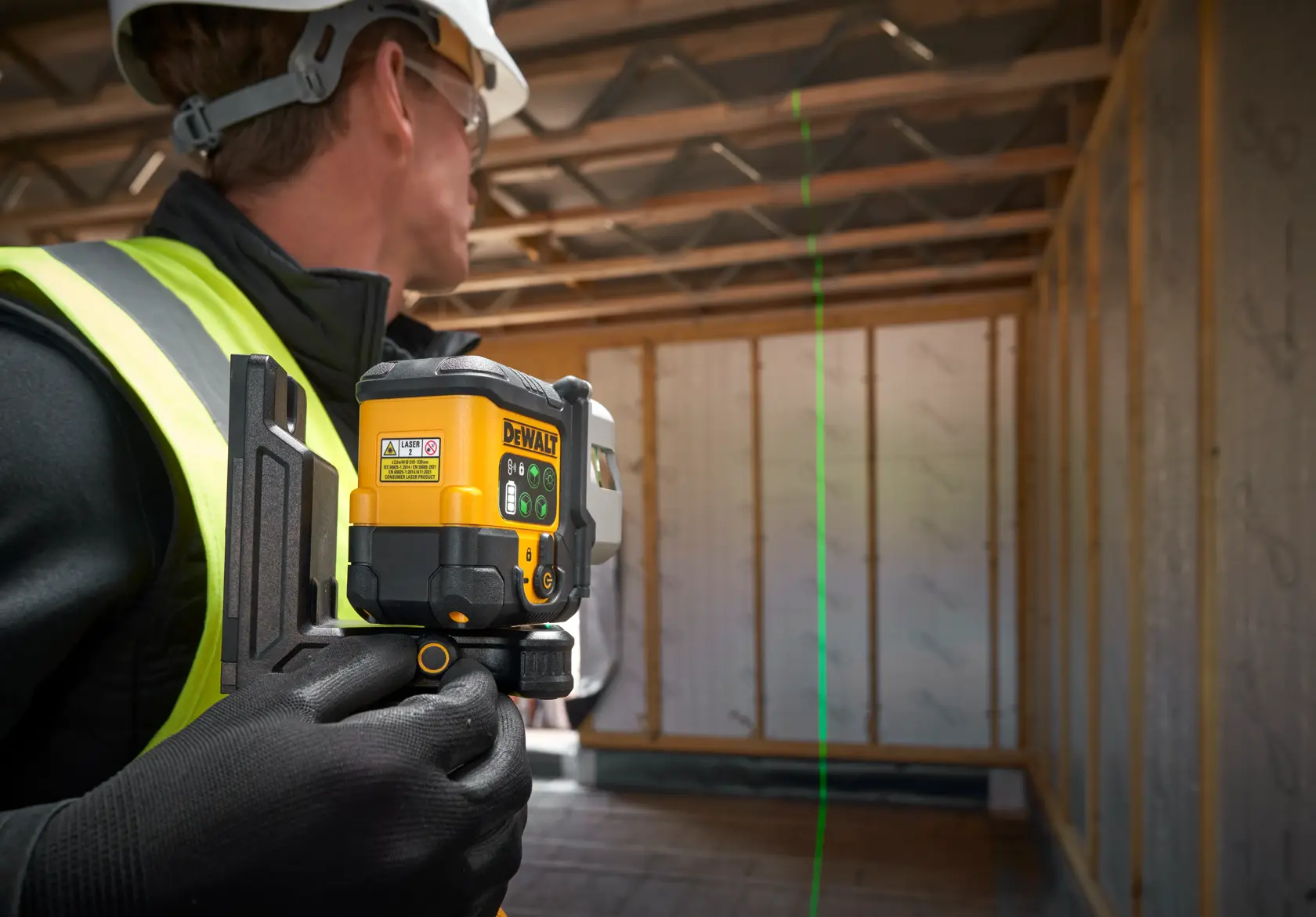 DEWALT laser level on tripod projects green line in construction site, worker marks wall alignment.