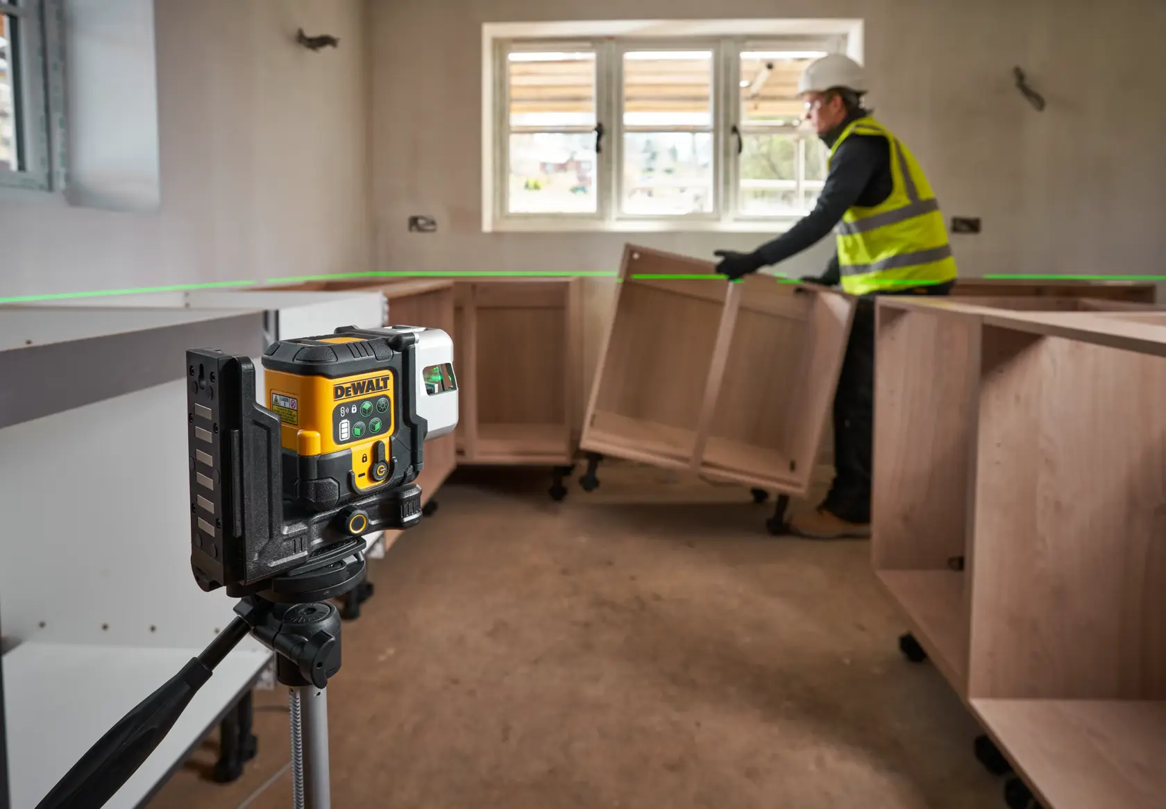 Worker uses a DEWALT green laser level for alignment in a building under construction.