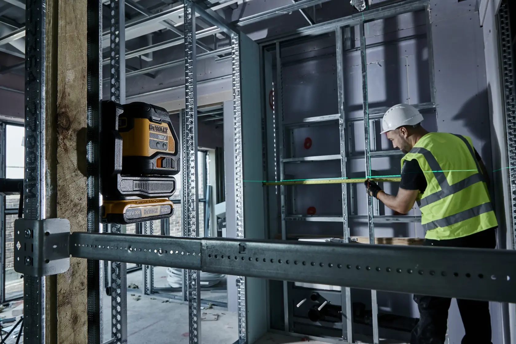 DEWALT laser level used at a construction site, worker in safety gear measuring distance with green laser line.