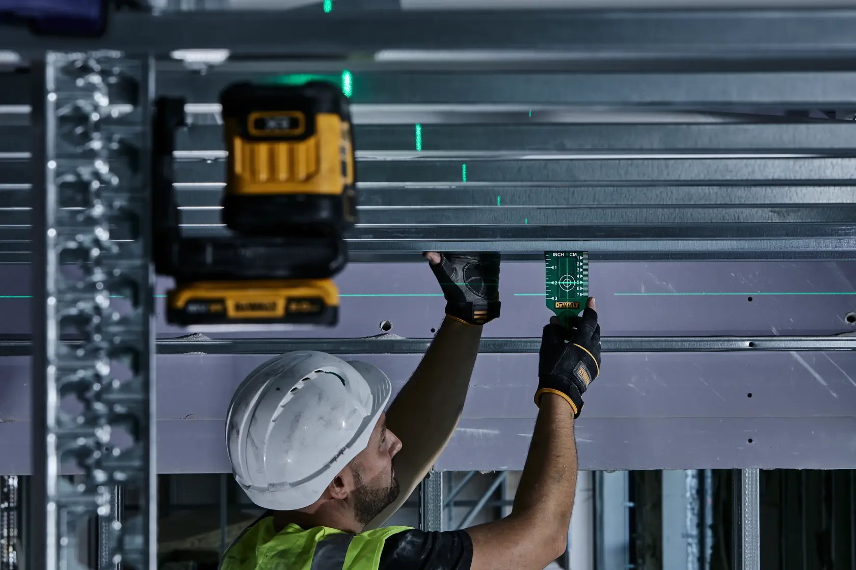 Worker uses DEWALT laser level DCLE34021 for construction alignment on metal beams.