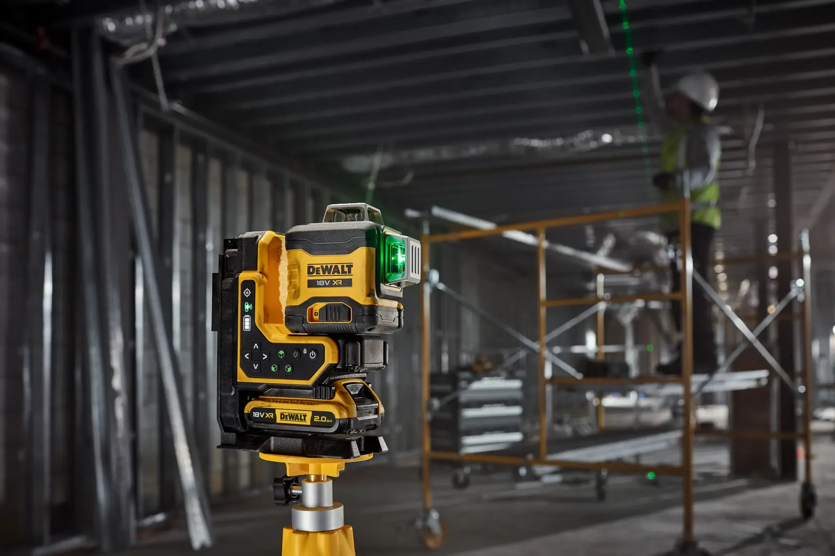 Niveau laser DEWALT fixé à une ossature métallique, lignes vertes projetées; ouvrier sur chantier.