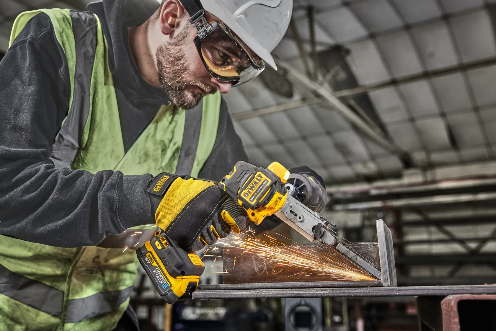 Worker uses DEWALT DCM200E2T tool to grind metal, creating sparks in an industrial workshop setting.