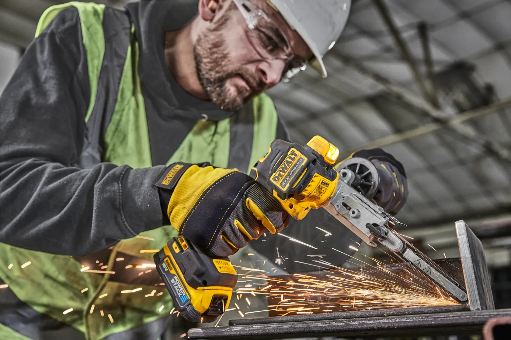 Worker using DEWALT cordless belt file tool on metal, creating sparks in an industrial setting.