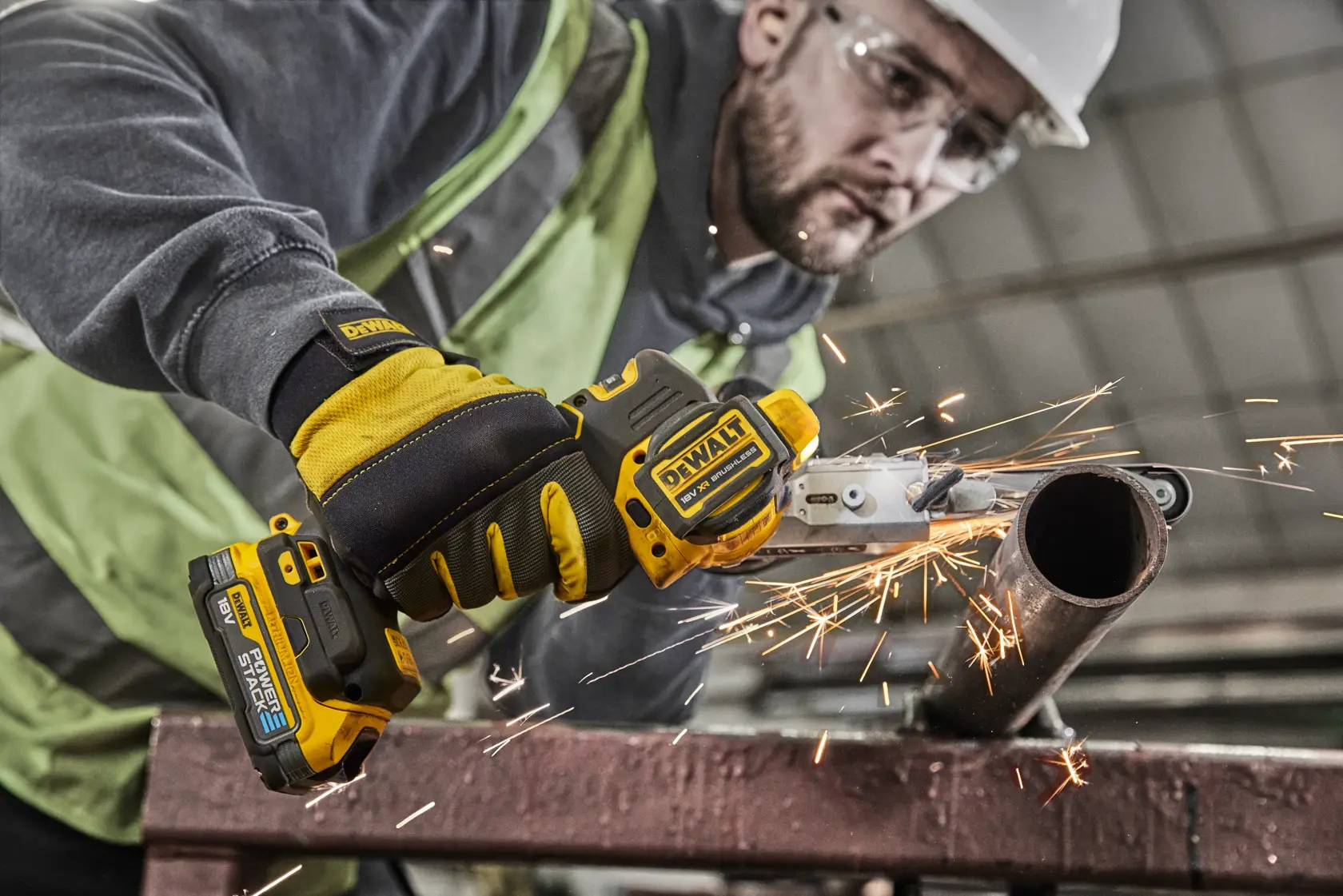 Worker uses DEWALT cordless metal cutter, sparks fly while cutting a steel pipe at work site.
