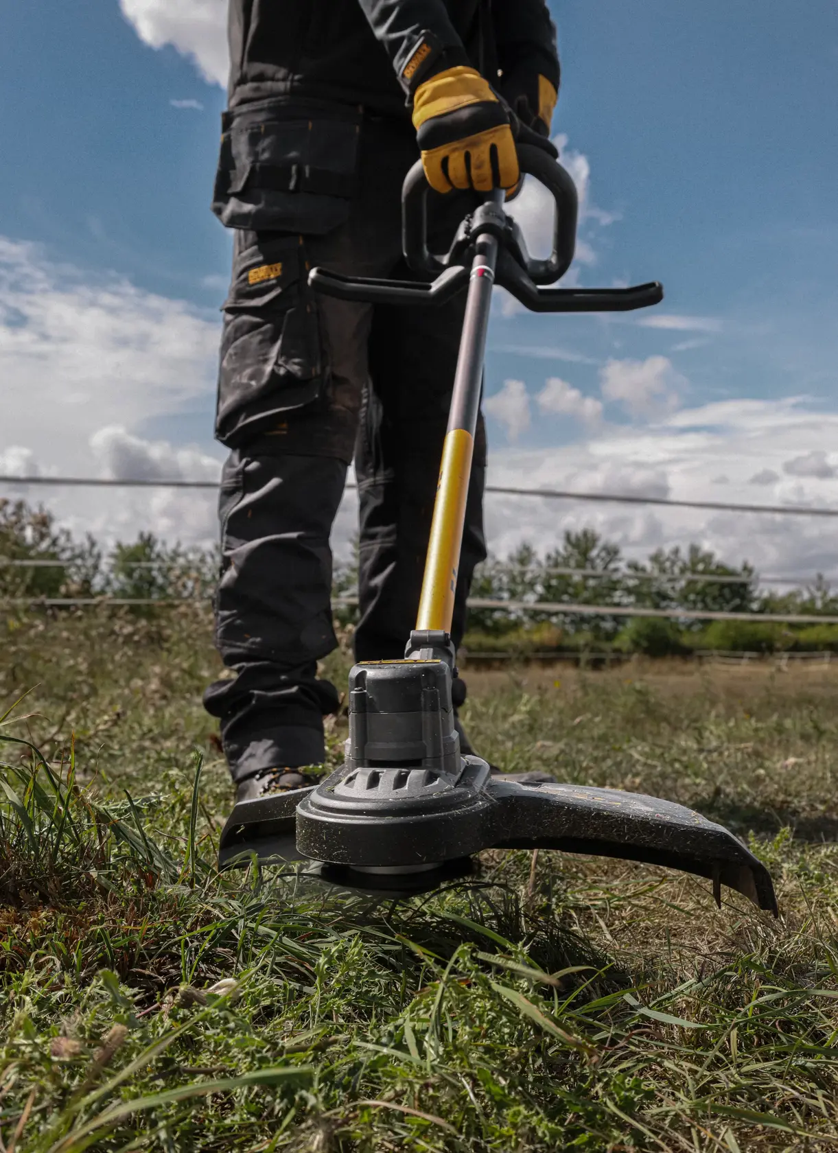 Persona usando una recortadora DEWALT inalámbrica en pasto alto al aire libre.