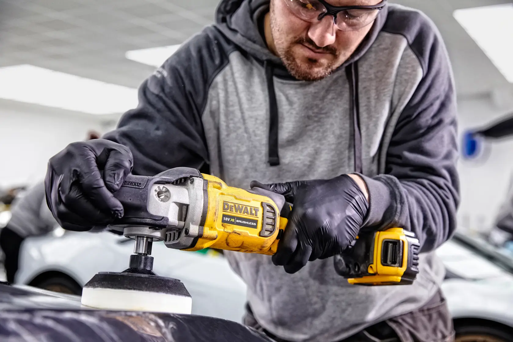 Persona usando pulidora DEWALT DCM849P2 en coche dentro de taller, lleva guantes.